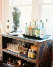 a navy and gold vintage home bar cabinet with chic decor, lots of wine bottles and glasses is a stylish idea for an eclectic space