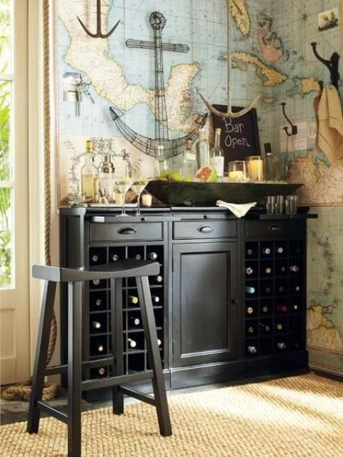 a stylish home bar nook with a world map on the wall, a black storage unit, candles, bottles and glasses and a black stool is a chic and lovely space for a travel fan