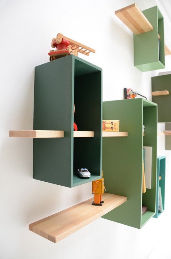 a wall-mounted bookcase in muted green shades with natural-colored shelves features much storage space in a creative way