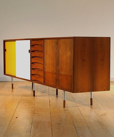 a large mid-century modern sideboard with stained drawers and doors, with white and yellow doors and tall and thin metal legs is a catchy solution with a contrasting touch