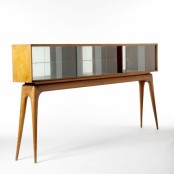 a light-stained mid-century modern sideboard on tall legs, with mirrror on the back and glass doors
