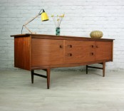 a rich-stained mid-century modern sideboard with doors and drawers with cutout knobws on tall legs for a mid-century modern living room