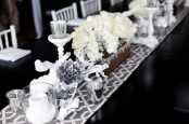 a black and white winter table setting done with a printed runner, white and silver blooms, candles and white branches