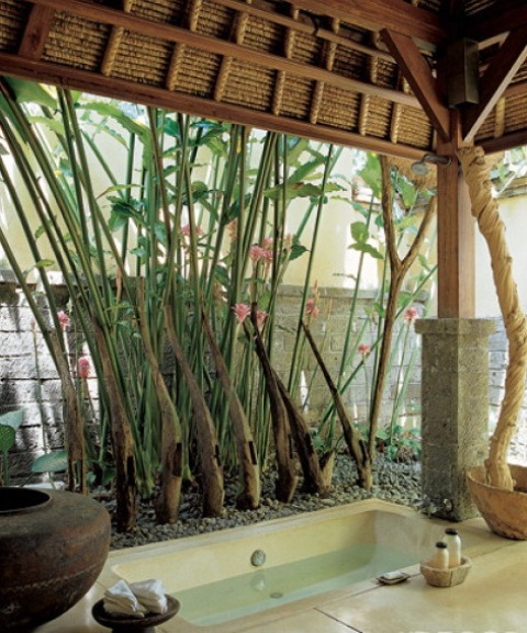 a zen-like outdoor bathroom with a built-in tub, pebbles, vases and living trees and greenery