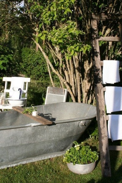 a rustic outdoor bathroom with a metal tub, potted greenery and living trees