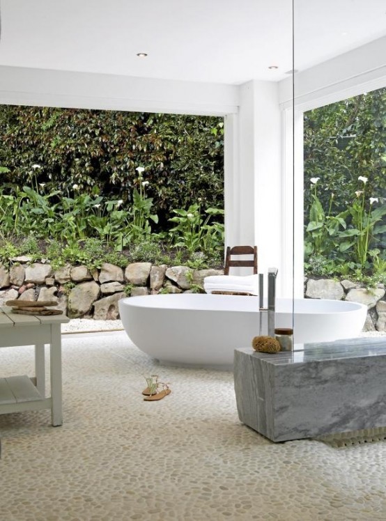 a contemporary outdoor bathroom with an oval tub, a marble bench and wooden tables