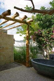 a rustic outdoor bathroom with a stone tub, a tile clad wall and floor and beams