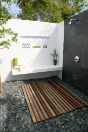 a minimalist outdoor shower with a pallet floor, pebbles, black and white walls and built-in shelves