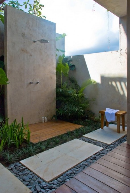 a welcoming outdoor shower with stone tiles, pebbles, tropical greenery and accessories