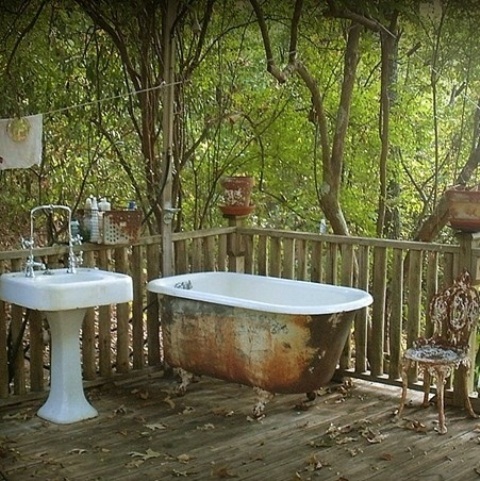 a shabby chic outdoor bathroom with a shabby bathtub and a free-standing sink