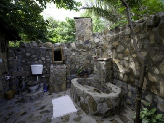 a rustic outdoor bathroom completely done with stone and a stone bathtub