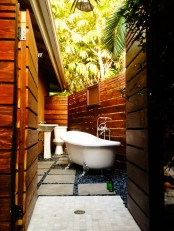 a small yet inviting outdoor bathroom and toilet in one, with dark pebbles on the floor