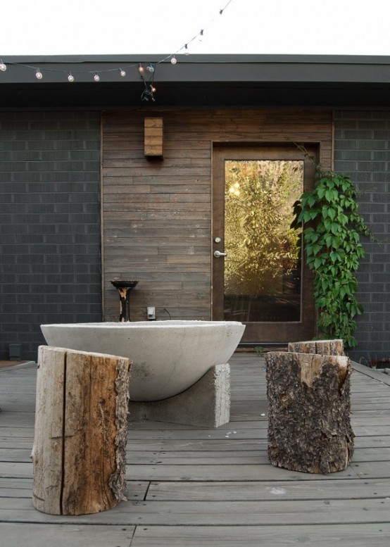 a rough outdoor bathroom space with a concrete tub and several stumps as side tables