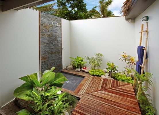 a welcoming outdoor shower nook with a wooden floor, a stone clad wall and much greenery planted here