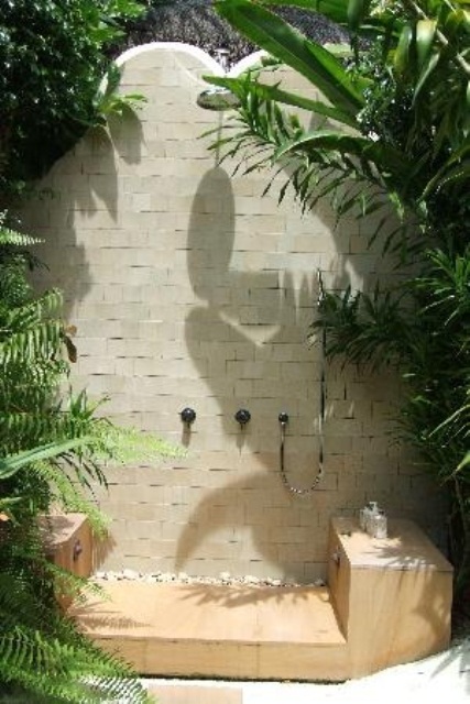 an outdoor shower with neutral tiles, a wooden stand and planted greenery