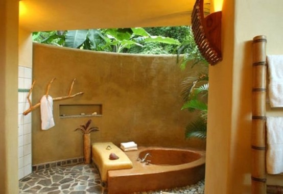 a bathroom with no roof, a stone wall and a concrete sinken bathtub plus greenery