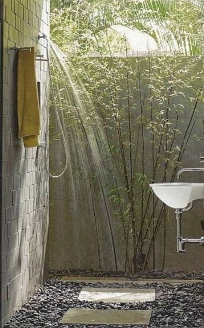 a simple outdoor shower with brick walls, pebbles on the floor, planted greenery and a sink