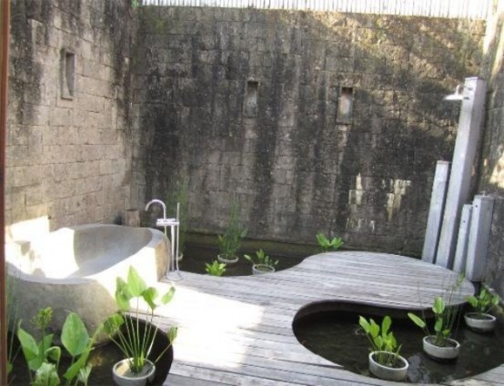 a modern and inspiring outdoor bathroom with a wooden floor, a stone tub and potted plants