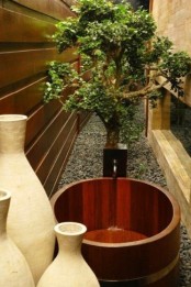 an outdoor Japanese bathroom with a wooden soak tub, a planted tree and vases