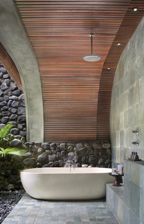 a contemporary outdoor bathroom with an oval tub, tiles and a stone wall