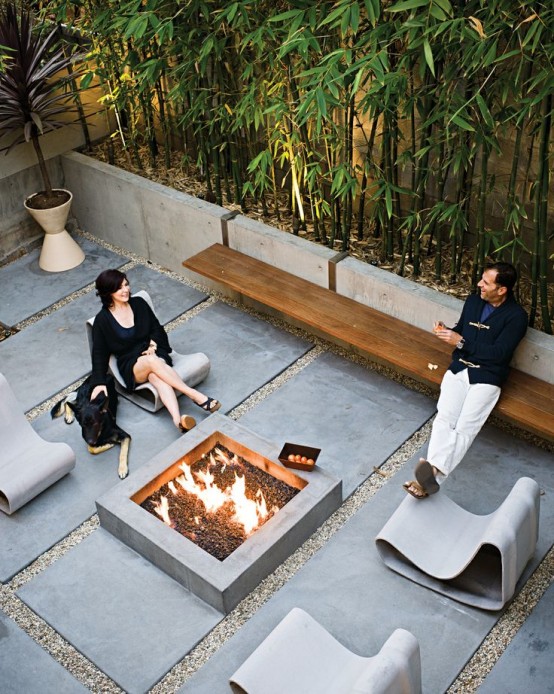 a contemporary terrace with a concrete fire pit, concrete loungers, a floating wooden bench and tall bamboo feels very edgy and cool