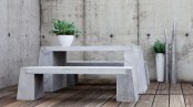 a modern rustic space with concrete walls, a concrete table and benches and a reclaimed wood floor plus potted greenery to enliven the space