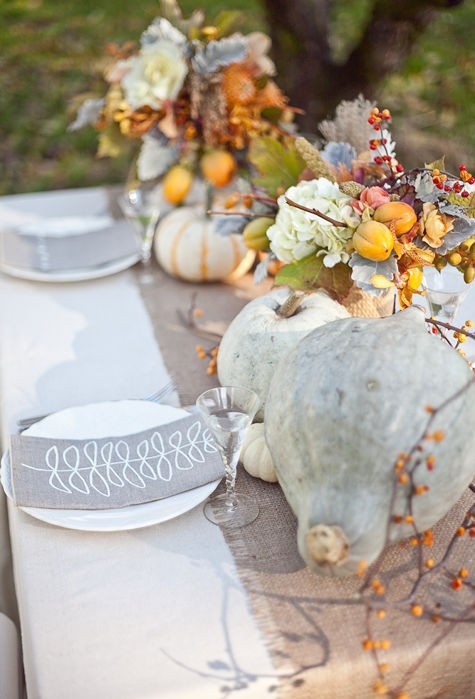 a pale Thanksgiving tablescape with a burlap table runner, grey napkins, grey pumpkins, a floral centerpiece with fruits