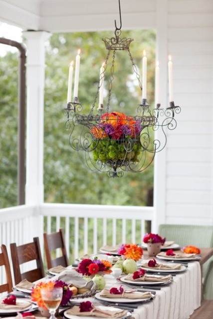 a colorful Thanksgiving tablescape with bright blooms, pumpkins and a bright floral decoration overheads