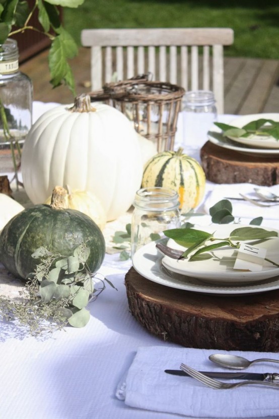 a nautral outdoor Thanksgiving table with white and green pumpkins, greenery and vine covered candleholders plus wood slices for placemats