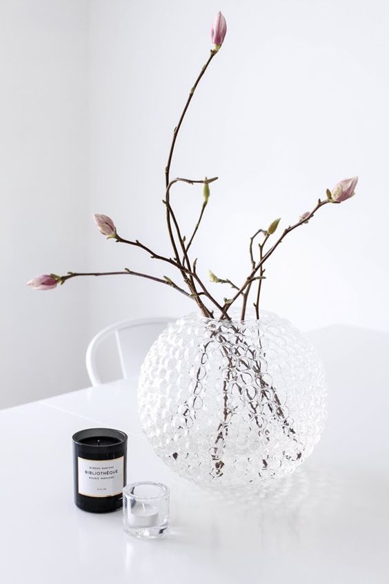 a glass sphere vase with blooms and some candles compose a simple and chic spring composition with a minimalist feel