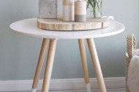 cute spring Scandi decor with a wood slice, wooden color block candleholders and candles, a stone house-shaped piece and white blooms in a vase