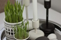 a Nordic tray with painted pebbles as eggs, potted wheatgrass and candles in black and white candleholders