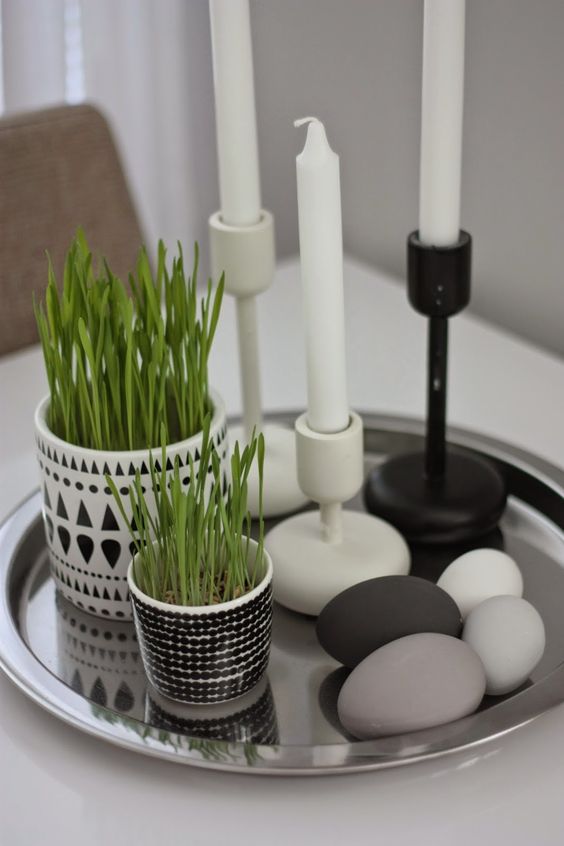 a Nordic tray with painted pebbles as eggs, potted wheatgrass and candles in black and white candleholders