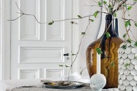 Nordic spring decor with a large bottle with greenery, some simple grey textiles and a shell covered vase