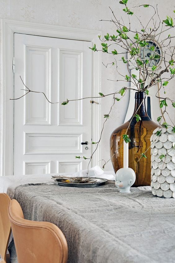 Nordic spring decor with a large bottle with greenery, some simple grey textiles and a shell covered vase