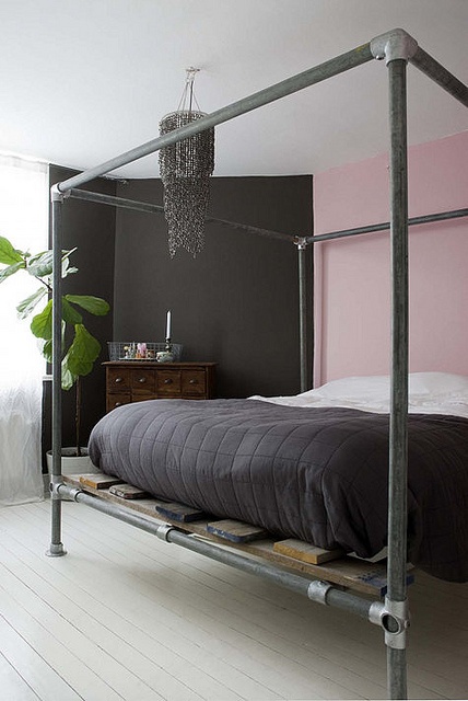 a contrasting bedroom with a black and pink wall, a bed with a pipe frame, black and white bedding and a bold black beaded chandelier