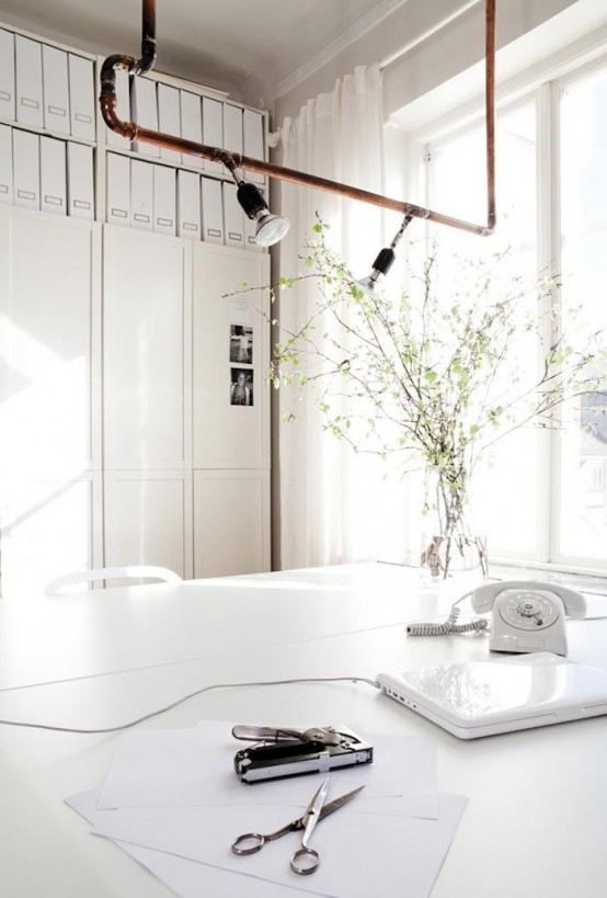 a white Scandinavian home office with file cabinets, a large desk and white chairs, a pipe and bulb pendant lamp over the desk for an unexpected touch