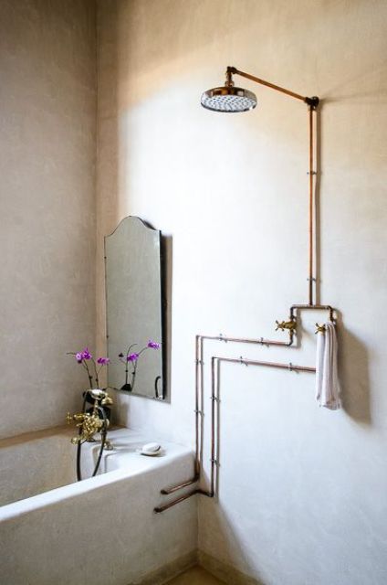 a neutral bathroom with a built-in tub, exposed pipe shower and a mirror of a refined and cool shape