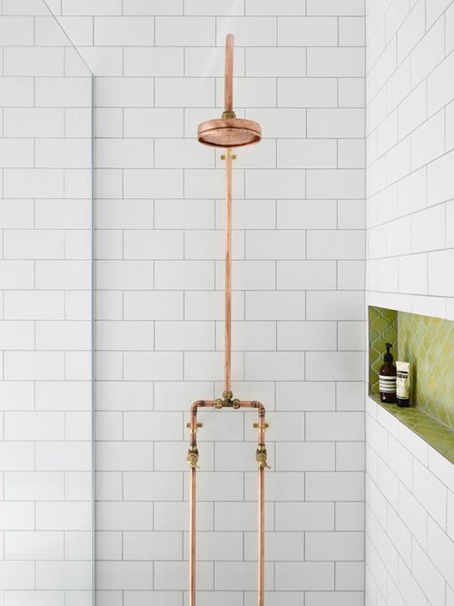 a modern shower space clad with white subway tiles, with a grene niche and gold exposed pipes of the shower itself is an eye-catchy space