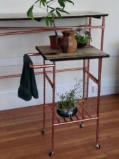 tables made of copper pipes and dark-stained wood are a great idea for an industrial or modern space, potted plants refresh the look