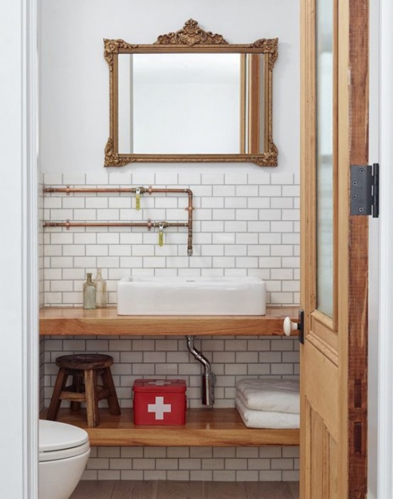 a small catchy powder room with white subway tiles, a floating wooden vanity, a mirror in a chic frame, exposed pipes just for decor