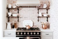 a vintage dove grey kitchen with shaker style cabinets, a vintage cooker, a vintage hood and open shelves plus a whitewashed brick backsplash