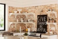 a white kitchen with shaker style cabinets and black handles, with open shelves, a whitewashed brick backsplash and a small kitchen island with a concrete countertop
