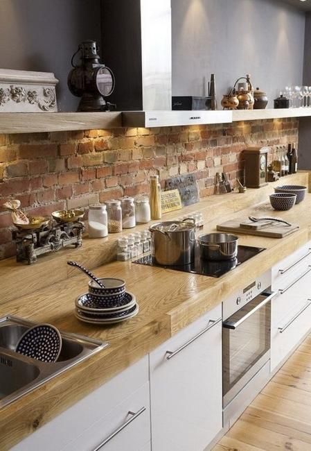 a lovely Scandinavian kitchen with sleek white cabinets, wooden countertops, a red brick backsplash, built in lights and open upper cabinets