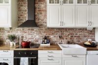 a small and pretty Scandinavian kitchen with shaker cabinets, butcherblock countertops, a black hood, a built-in cooker and a red brick backsplash that adds interest and eye-catchiness to the space