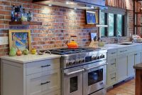 a grey kitchen with shaker style cabinets, grey countertops, a red brick backsplash, a vintage metal hood, open shelves and lots of natural light