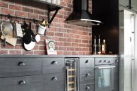 a stylish black kitchen with elegant cabinets, a red brick backsplash and black appliances looks bold, contrasting and super chic
