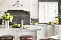 a white farmhouse kitchen with shaker style cabinets, with a glossy black brick backsplash that is extended on the second wall