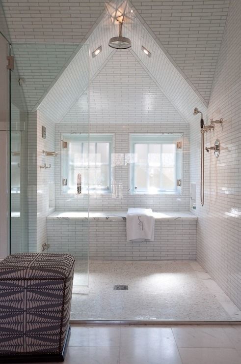 a neutral attic bathroom with white tiles highlighted with black grout, metallic fixtures and a large upholstered pouf