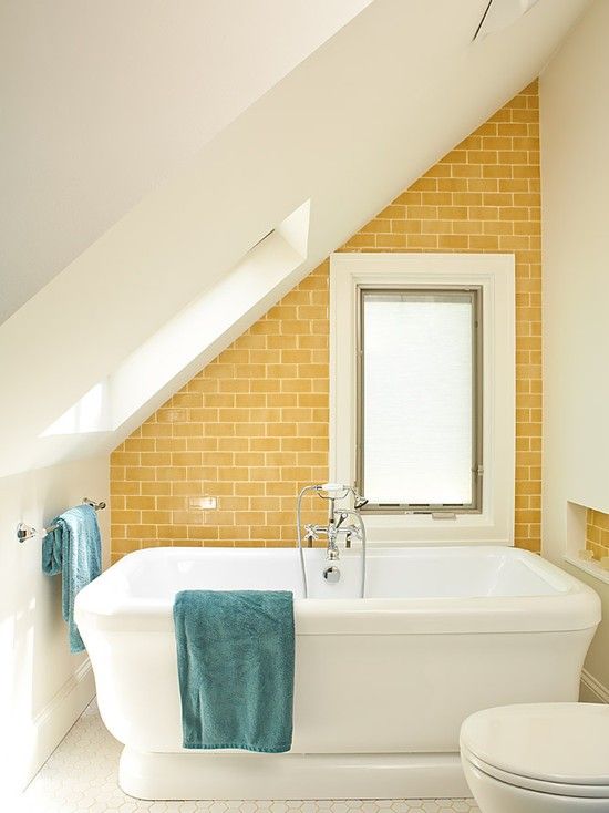a bright attic bathroom with a yellow statement wall, a large tub and blue towels